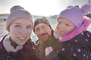 Vanessa (links) mit ihrem Mann (Mitte) und ihrer Tochter (rechts). Alle tragen Winterkleidung und Mützen. Im Hintergrund ist ein schneebedecktes Feld zu sehen. 