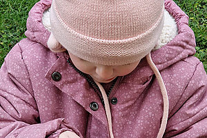 Kleines Mädchen mit rosa Winterjacke und rosa Mütze. Ihr Gesicht ist nicht zu erkennen. Sie ist etwa drei Jahre alt. 