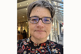 Porträt von Anne (im Hintergrund sieht man eine Einkaufsstraße). Sie 51 Jahre alt und hat Mukoviszidose