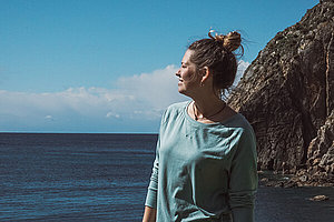 Denise am Meer Denise steht am Meer. Im Hintergrund sieht man einen Felse, den blauen Himmel und das Meer.