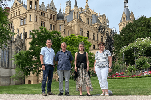 Regionalgruppen-Sprecher aus Mecklenburg-Vorpommern (von links nach rechts): Herr Ehret (Regionalgruppe Schwerin), Herr Walter (Regionalgruppe Neubrandenburg), Frau Bremer (Regionalgruppe Greifswald), Frau Worschech (Regionalgruppe Schwerin), sie stehen vorm Schweriner Schloss. 