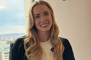 Sophie Grace Holmes ist Ultraläuferin - und hat Mukoviszidose. Porträt von Sophie Grace Holmes - lange blonde Haare, Lächeln, im Hintergrund sieht man Franfurt von oben aus einem Fenster.