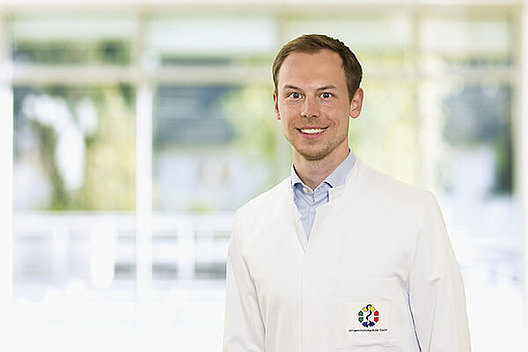 PD Dr. med. Marcel Opitz im Labor. Er trägt einen weißen Kittel über einem hellblauen Hemd. Foto: Mukoviszidose e.V.