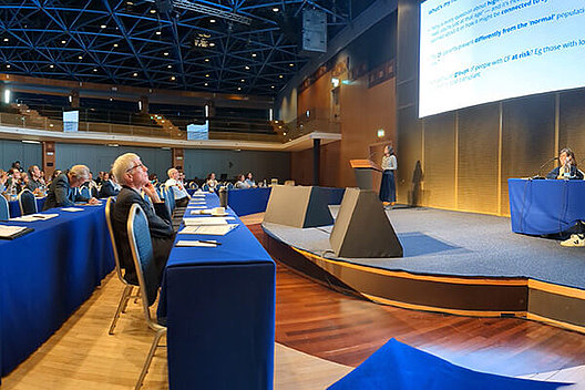 Symposium der Patientenorganisationen auf der ECFS Basic Science Konferenz auf Malta Blick von der Seite in einen Konferenzraum, Menschen im Publikum schauen auf die Bühne.