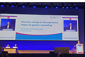 Bühne auf einer Konferenz. Auf der an die Wand geworfenen Folie liest man: How does change in life expectancy impact on genetic counseling. - Julia Hentschel bei ihrem Vortrag auf der europäischen CF-Konferenz in Glasgow. 