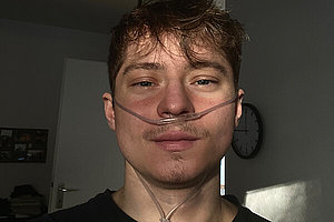 Jonas (junger Mann, dunkele Haare, dunkle Kleidung) hat eine Sauerstoffbrille auf. 