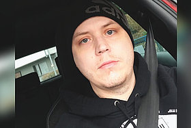 Klaus Dieter sitzt angeschnallt im Fahrersitz eines Autos. Er trägt eine schwarze Mütze. 