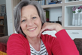 Porträt von Simona mit roter Strickjacke und gestreiftem T-Shirt. Simona berichtet regelmäßig auf unserem Blog.