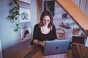 Frau sitzt an einem Apple-Laptop und lächelt. 