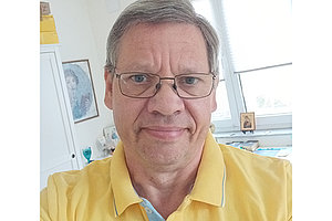 Porträt von Thomas: Mann um die 60 Jahre alt, trägt ein gelbes Polo-Shirt, im Hintergrund sieht man ein Fenster. 