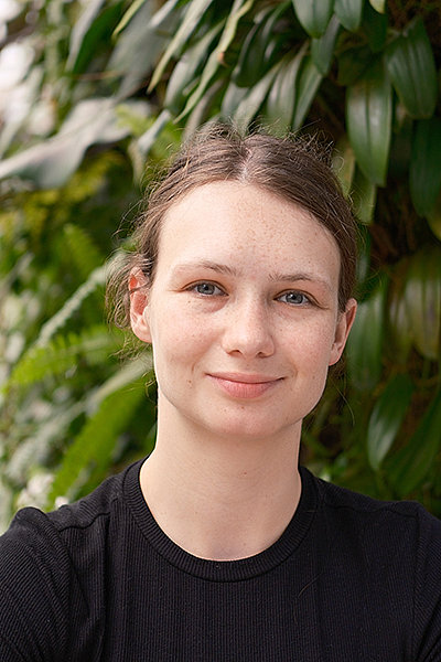 Svea Andresen Porträt von Svea Andresen: junge Frau, im Hintergrund sind Bäume und Blätter zu sehen, die Haare sind zu einem Pferdeschwanz gebunden.