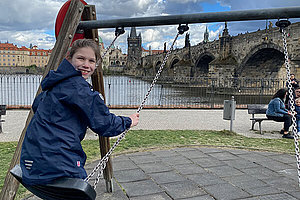 Zehnjähriges Mädchen auf einer Schaukel, im Hintergrund sind ein Fluss und eine Brücke zu sehen. 