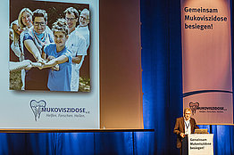 Stephan Kruip, Vorstandsvorsitzender des Mukoviszidose e.V. am Podium, im Hintergrund sieht man einen Teil einer PowerPoint-Folie