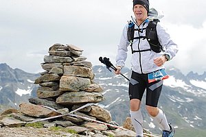 Mann in Sportkleidung und Wanderstöcken auf einem Berggipfel.