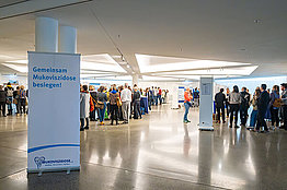 Kleine Gruppen von Menschen stehen in einem größeren Foyer um Poster gruppiert, Blick in die Posterausstellung der DMT 2023.