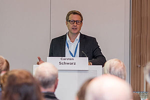 Mann auf dem Podium beim Vortrag, Hinterköpfe sind zu sehen. Prof. Carsten Schwarz, ärztlicher Leiter des CF-Zentrums Westbrandenburg in Potsdam, auf der Deutschen Mukoviszidose Tagung 2023. Foto: Britta Leonhardt-Kuschner