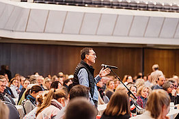 Blick ins Publikum beim Plenum der DMT 2023, ein Mensch steht und stellt eine Frage