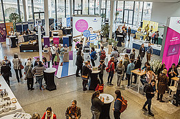 Von oben geschossenes Foto, man sieht viele Menschen in einer Halle mit Informationsständen von Unternehmen der gesundheitsbezogenen Industrie. Blick in die Industrieausstellung der Deutschen Mukoviszidose Tagung. 