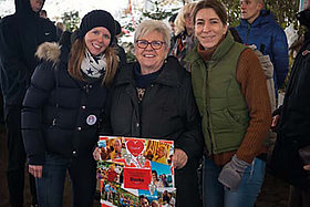 Drei Frauen, zwei jünger, die Frau in der Mitte etwas älter, stehen auf dem Weihnachtsmarkt zusammen. 