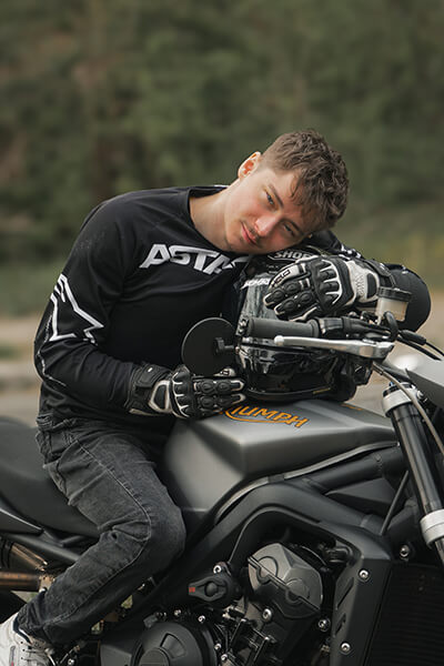Junger Mann, dunkel gekleidet, schmiegt sich fast an sein Motorrad (silber-grau-schwarz). Jonas hat Mukoviszidose und ist leidenschaftlicher Motorradfahrer.