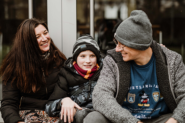 Familienfoto: Mutter, Sohn (11 Jahre) und Vater in Winterkleidung vor einem Fenster