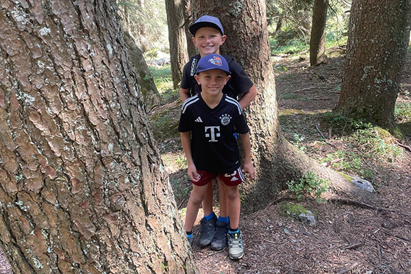 Zwei Jungs mit dunklen Fußballtrikots im Wald zwischen Bäumen