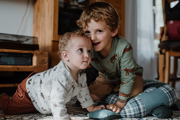 Zwei kleine Kinder, eines knapp ein Jahr alt, eines vielleicht drei Jahre alt, auf allen Vieren, sie berühren sich am Kopf. 