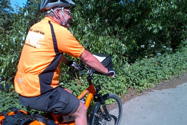 Mann mit orangener Fahrradkleidung fährt auf seinem Fahrrad. Man sieht ihn nur von hinten. 