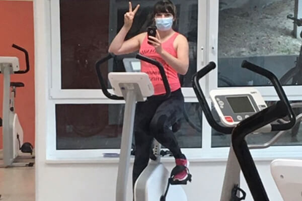 Eine Frau mit einer OP-Maske trainiert auf einem Ergometer.