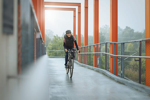 Eine Frau fährt Fahrrad auf einer Brücke - Sport ist bei Mukoviszidose wichtig. 