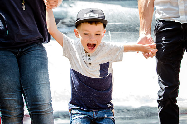 Lachendes Kind an den Händen der Eltern. Beim Kindergartenbesuch stellen sich für Eltern von Kindern mit Mukoviszidose viele Fragen. 