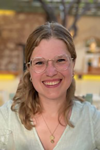 Cara Övermöhle Junge blonde Frau lacht in die Kamera, sie trägt eine Brille, ihre Haare sind lang. Sie trägt ein helles Shirt.