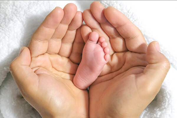 Babyfuß und große Hände. Bitten Sie Freunde und Verwandte zur Geburt oder zur Taufe um Spenden für Menschen mit Mukoviszidose. 