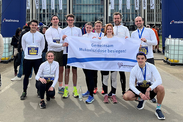 Mitarbeitende des Frankfurter Ardian Büros nach dem erfolgreichen Frankfurter Halbmarathon - mit Banner des Mukoviszidose e.V. 