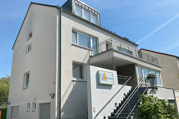 Außenansicht von Haus Schutzengel in Hannover: weißes, dreistöckiges Haus, blauer Himmel, Bäume mit grünen Blättern